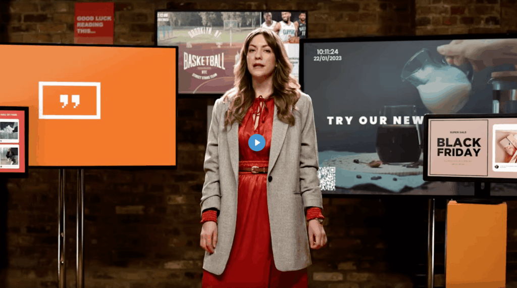 Presenter standing in front of several digital signage screens showing promotions and live content